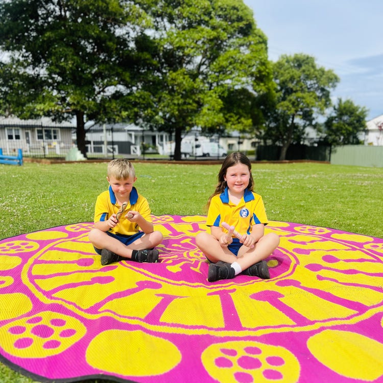 A girl and boy playing clapsticks on our Yarning mat